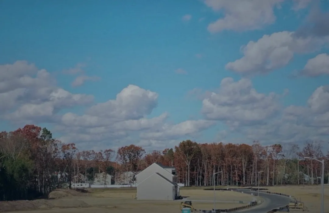 A house under construction in Fox Run at Mullica Hill, with the neighborhood street and open land behind it.