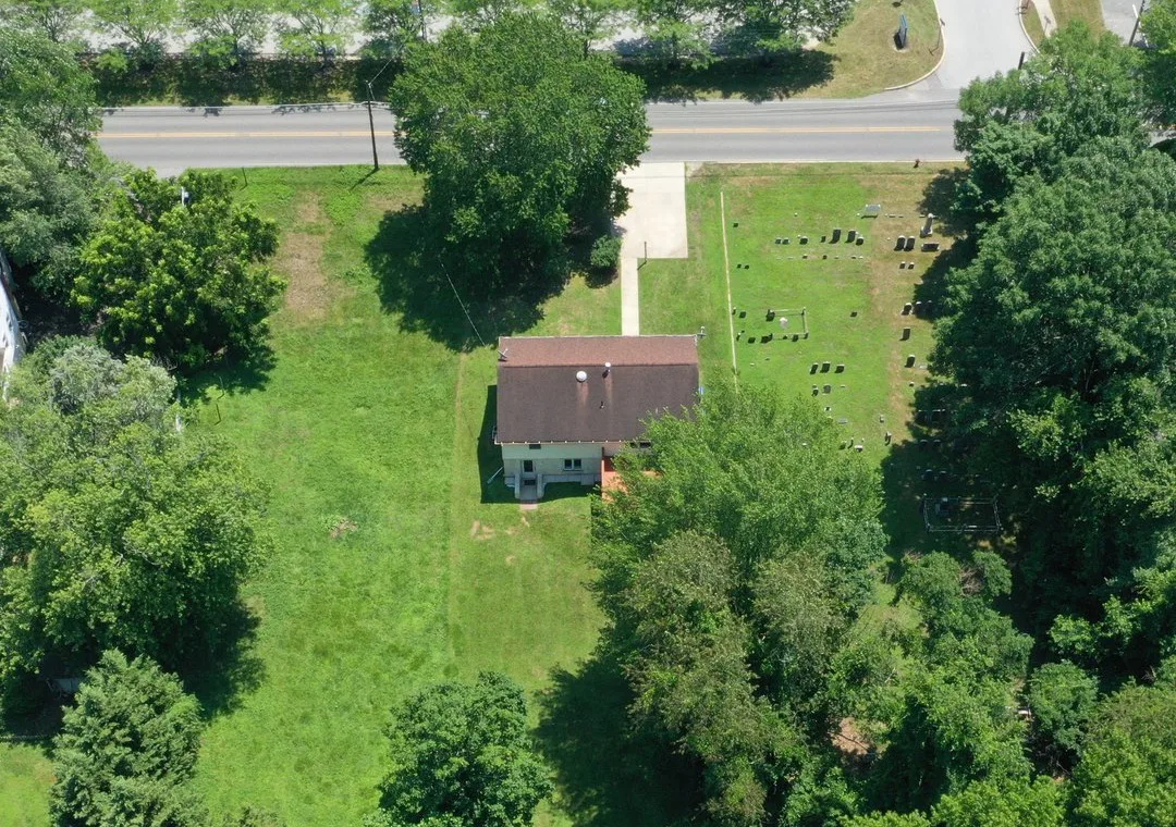 An overhead view of a deep lot with a small house near the road and trees along both sides