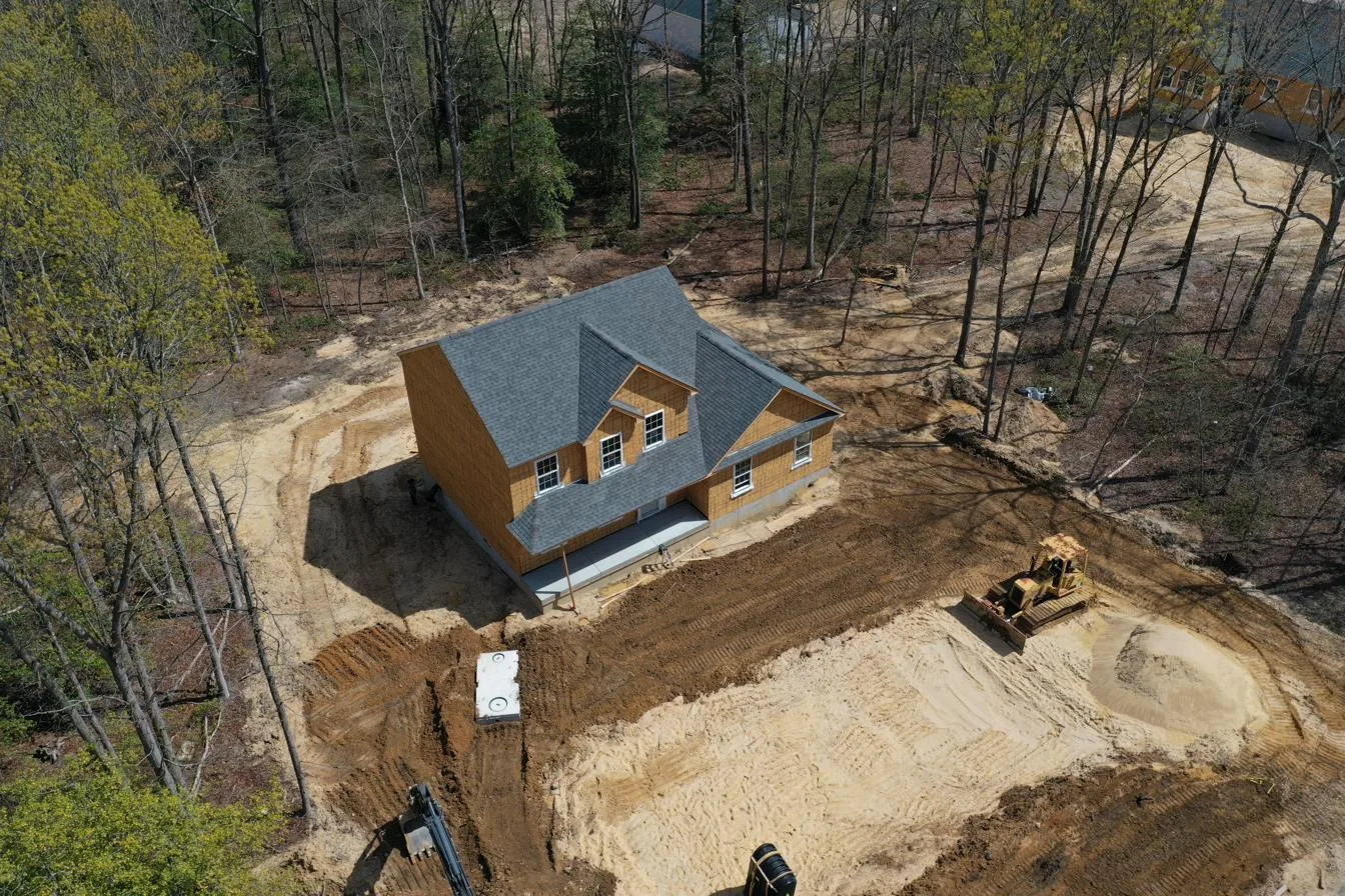 New construction colonial under roof framing at a South Jersey homesite — drone view showing graded lot, septic install, and site work in progress
