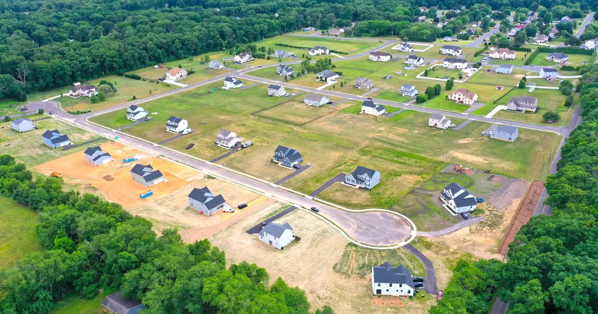 An aerial view of a new subdivision, lots graded along a cul-de-sac with homes at several stages of construction