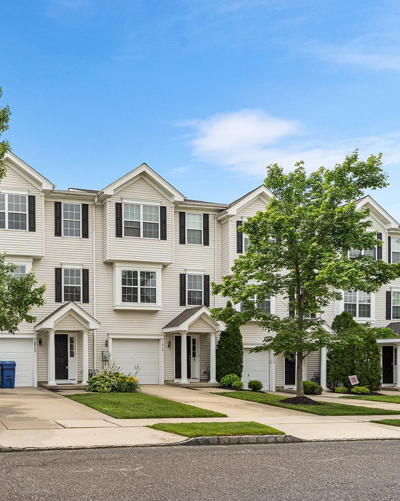 A row of new three-story townhouses with white siding and garages along a quiet street