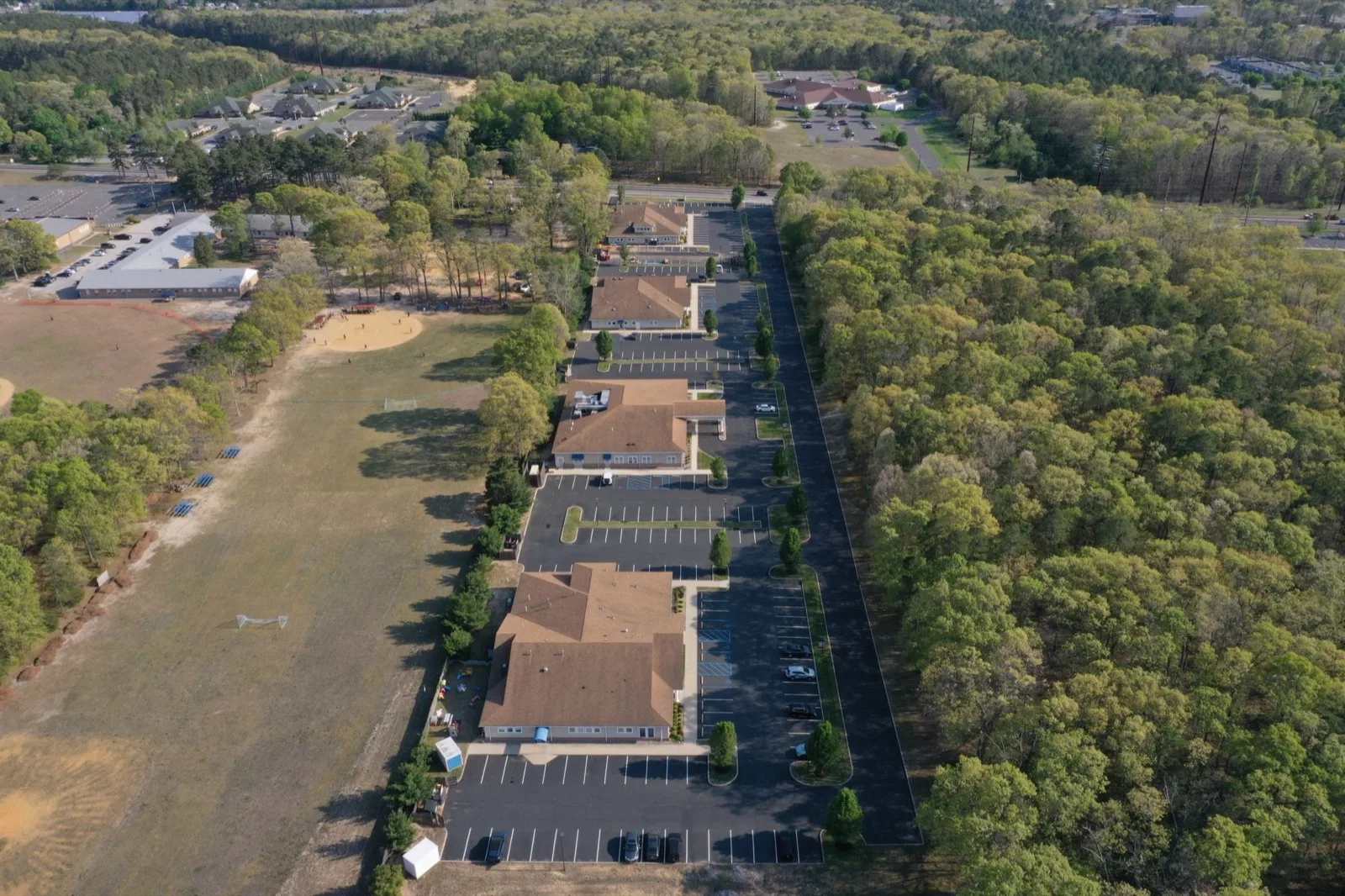 Aerial view of woods and an open field on either side of a row of low office buildings in Vineland
